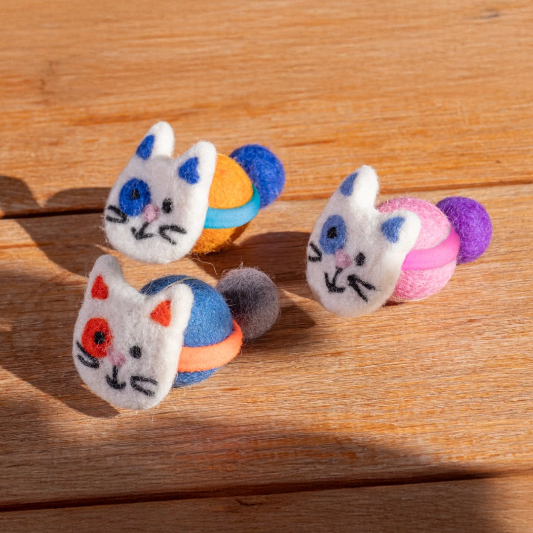 Drei bunte Spielzeuge in Katzenform auf einer Holzunterlage