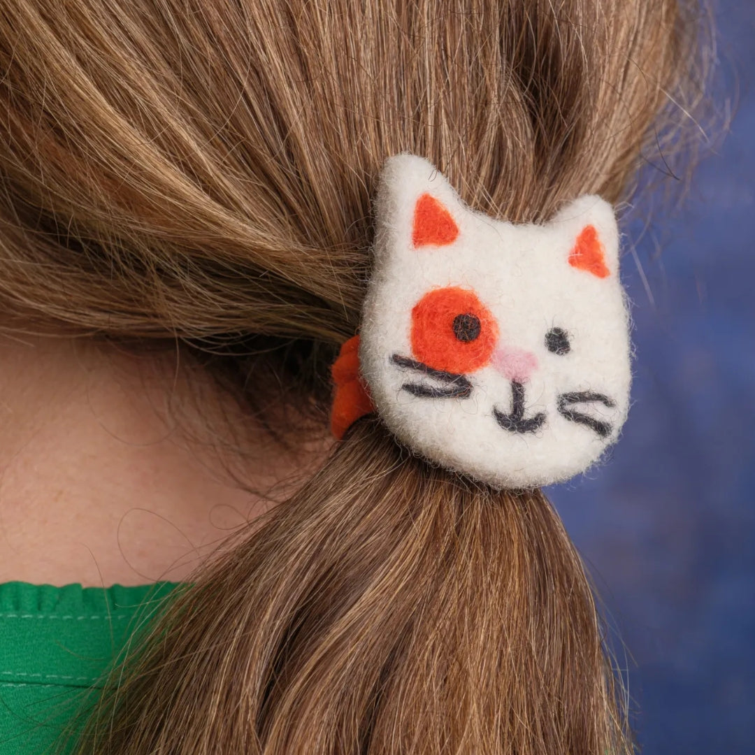 Eine katzenförmige Haarspange im Pferdeschwanz einer Person vor blauem Hintergrund